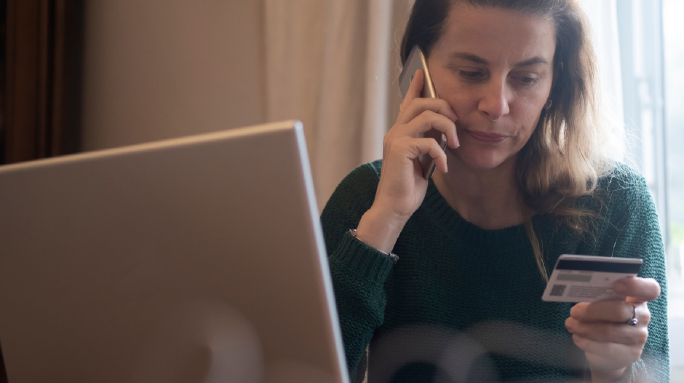 A woman with a mobile phone to her ear holding a credit card sat next to an open laptop