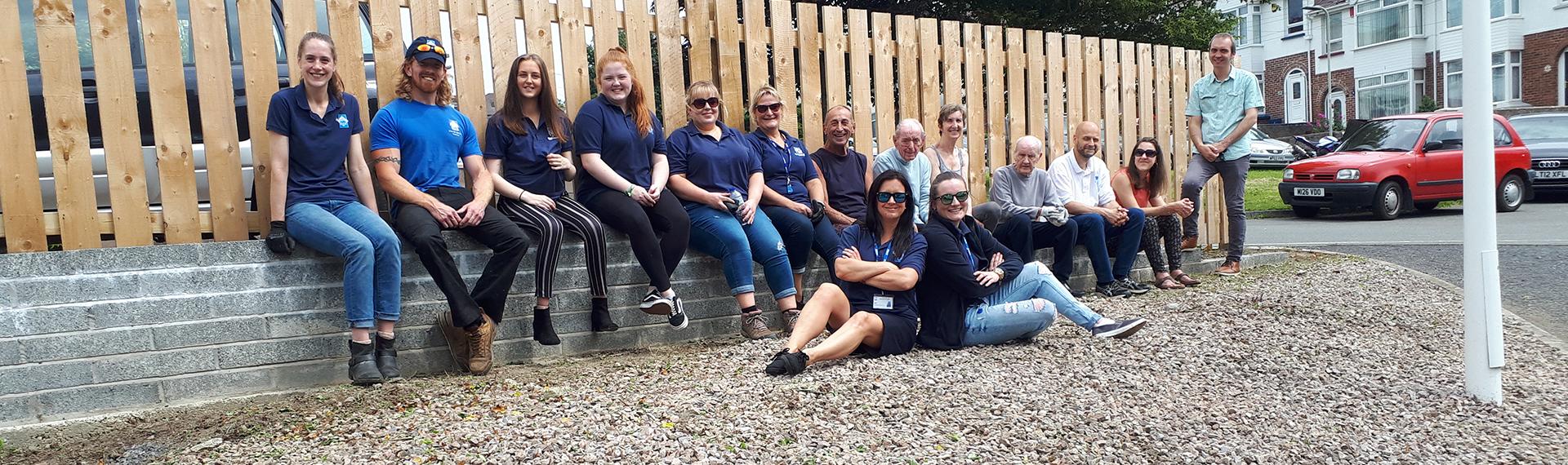 Clean Up Day 15 NDH staff resting on a wall with fencing