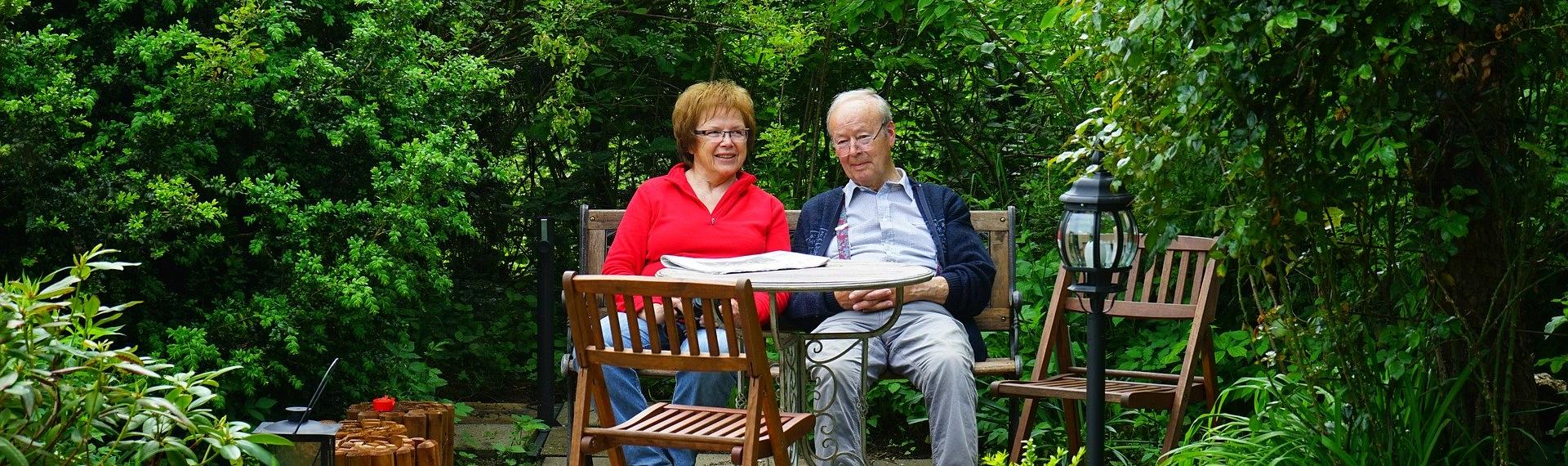 Garden; two people sitting in secluded garden at wooden table and chairs