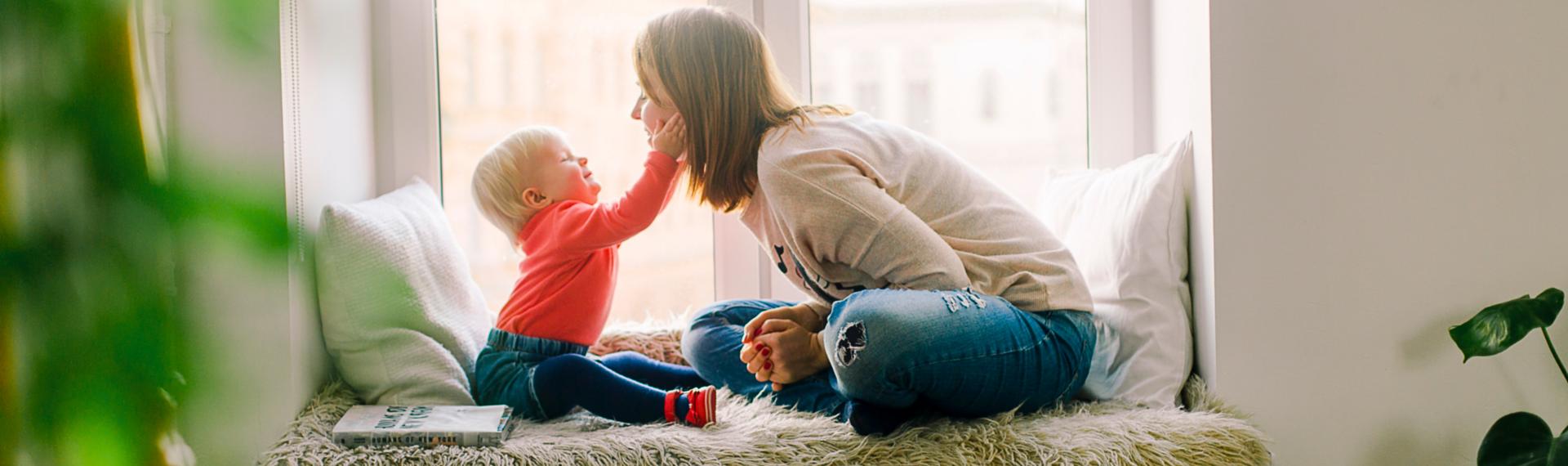 Mother and baby sitting on window seat; baby touching her face